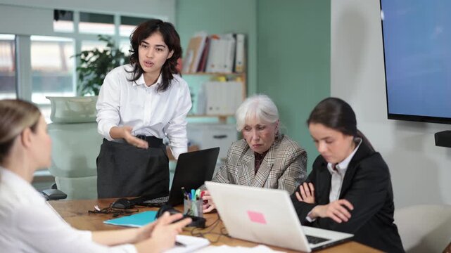 Young woman stands at office desk and scolds group of upset women in office