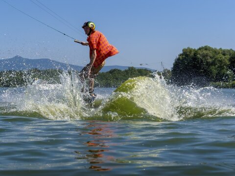 Young casual man with flapping shirt on wakeboard jumping into the lake, water ski and wakepark, Str&aacute;ž pod Ralskem, Czech Republic