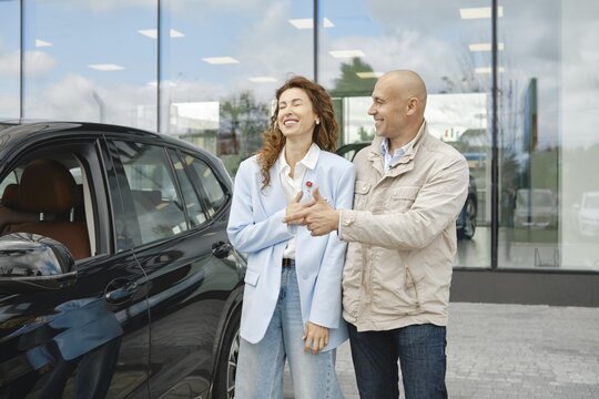 A couple is happily engaged in a conversation while selecting a new car at a dealership. The woman smiles as she interacts with her partner, who gestures toward the vehicle, suggesting its features