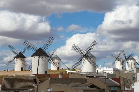 Several mills in a rural area, with old buildings in the foreground and a cloudy sky above, Campo de Criptana, Ciudad Real province, Castilla-La Mancha, Route of Don Quixote, Spain