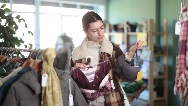 Woman in the store compares sets of underwear, carefully choosing the appropriate option among the assortment. Armenian woman buys a comfortable bra in store. High quality 4k footage