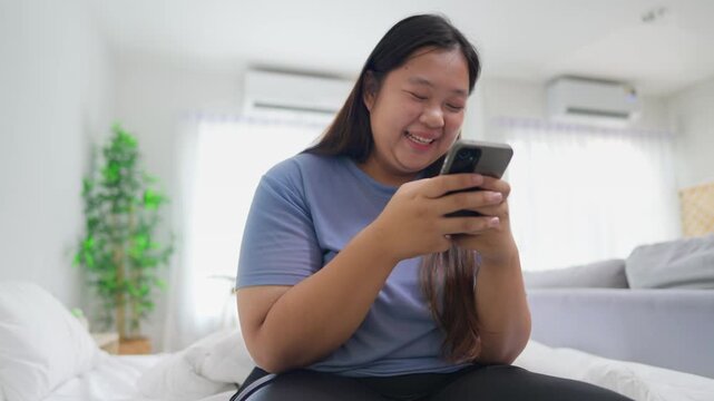 Asian young plus-size woman using smartphone in cozy room at home.