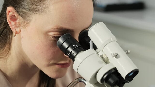 Gynecologist examines Pap test sample through microscope in close view. Specialist studies specimen carefully continuing detailed analysis