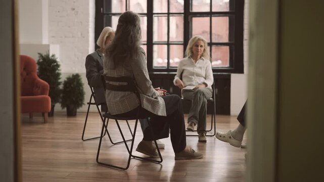 Senior woman talking about divorce or psychological troubles in group therapy. Modern mutual support group for people in difficult life situation, psychological help and supporting, ladies in circle