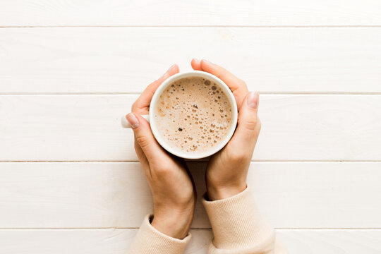 Minimalistic style woman hand holding a cup of coffee on Colored background. Flat lay, top view cappuccino cup. Empty place for text, copy space. Coffee addiction. Top view, flat lay