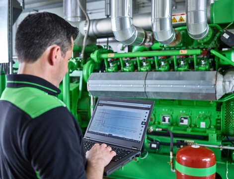 Combined heat and power plant, worker using laptop in front of gas engine