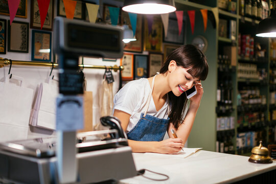 Smiling woman on the phone in a store taking notes
