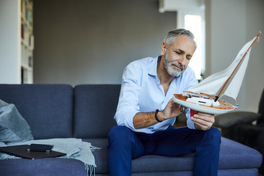 Mature man holding model sailboat at home