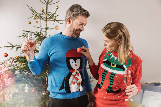 Two people with ugly Christmas sweaters laughing in front of tree