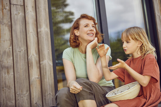 Smiling mother talking with daughter while sitting outside tiny house