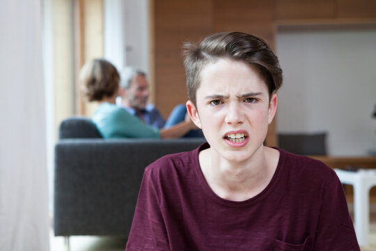 Portrait of angry teenage boy at home with parents in background