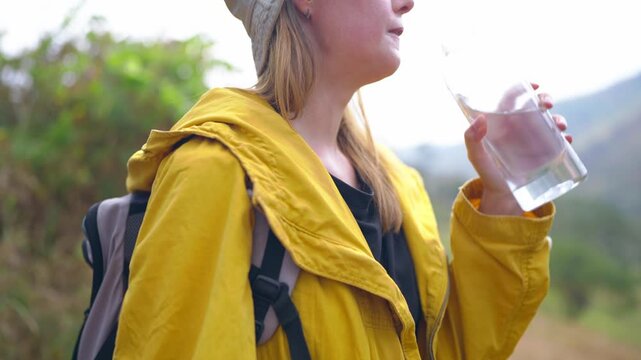 Caucasian female hiker drinking water while walking on trail in mountains. 
