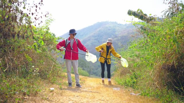 Two hikers collecting trash while walking along a mountain trail. 