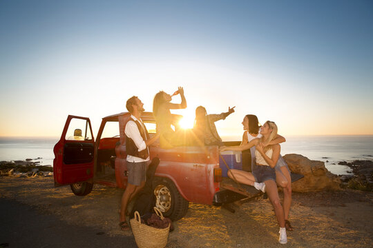 Happy young people outside pick up truck at the coast at sunset