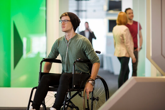 Young man in wheelchair listening to music in office