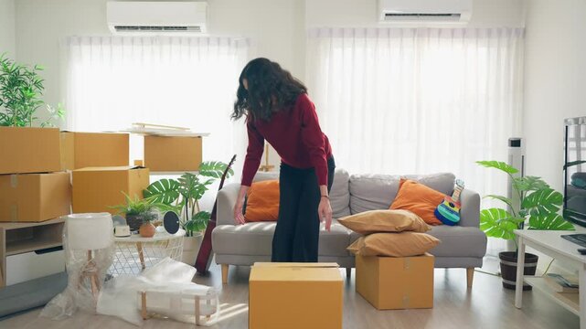 Young Hispanic woman arranging furniture and unpacking boxes in house. 