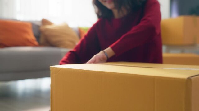 Close up of young woman arranging furniture and unpacking boxes in house.