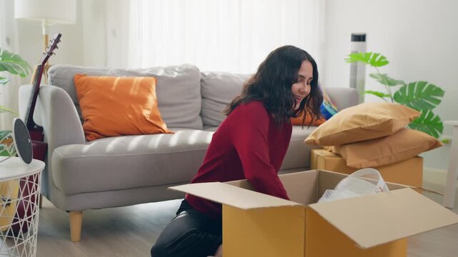 Young Hispanic woman arranging furniture and unpacking boxes in house