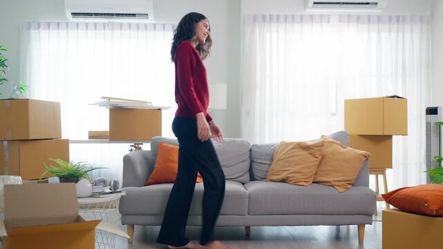 Young Hispanic woman arranging furniture and unpacking boxes in house. 