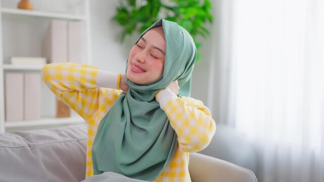 Asian Muslim woman stretching body on comfort sofa in living room at home. 