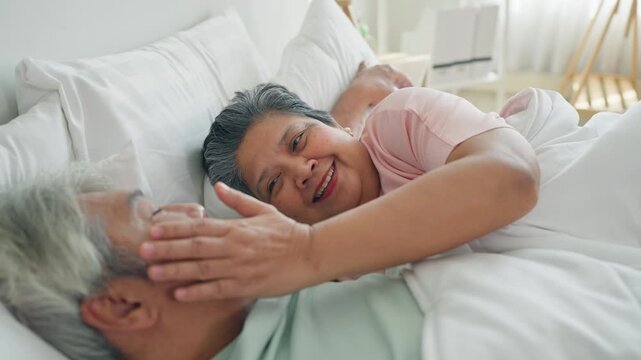 Asian senior elderly couple lying down on bed and talking to each other. 