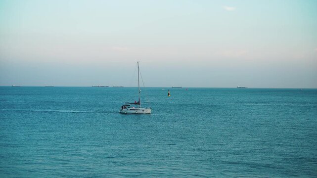 A small sailboat drifts on glassy blue ocean waters under a soft pastel twilight sky, with distant vessels on the horizon.