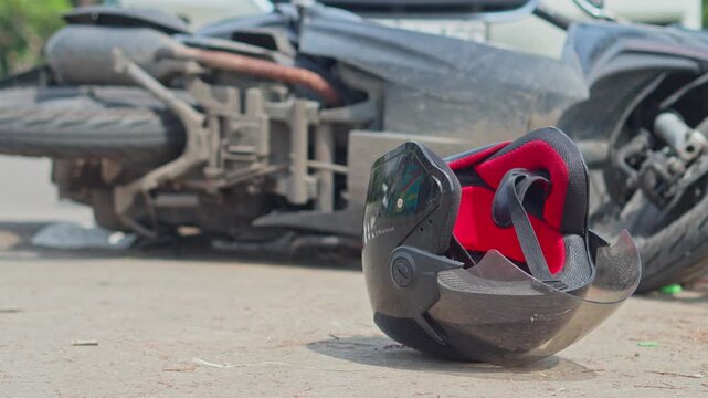 Black motorcycle helmet lies on road next to crashed motorbike after traffic collision