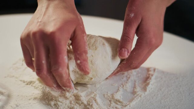 Hands knead dough on floured surface. Fingers press down, shaping soft, elastic dough. Flour dusts workspace. Focus on tactile, rhythmic motion. Ideal for recipes, baking tutorials