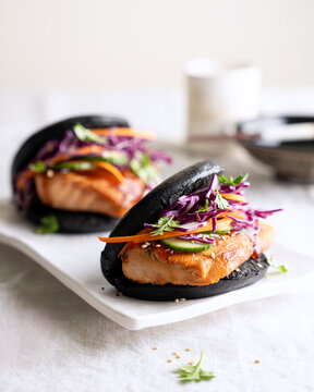 Black salmon bao buns with purple cabbage slaw on white ceramic plate