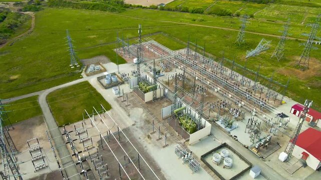 High voltage electrical substation with power transformers. Insulators. And pylons for energy transmission. Surrounded by a lush green countryside. Showcasing a critical component of power generation