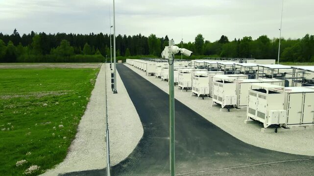 Aerial perspective of an industrial battery energy storage system facility with rows of modular containers and security cameras for sustainable power grid support and renewable resource management