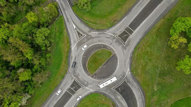 Aerial drone slow zoom-out revealing busy road junction with constant vehicle movement and intricate road pattern from above. Widening perspective showing traffic circulation and surrounding