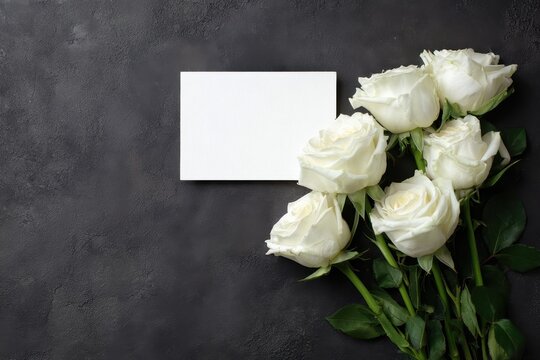 Top-down photograph of white roses with a blank condolence card on a dark background