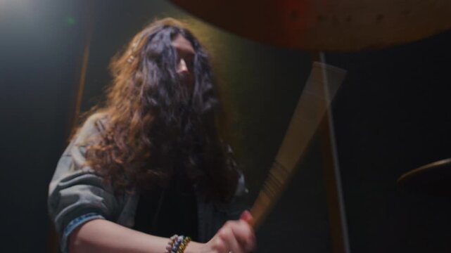 Portrait: female with long curly hair plays the drums. Girl is rehearsing in a studio with drumsticks. Face of a beautiful musician girl, showcasing skill and energy. Underground indie slow motion
