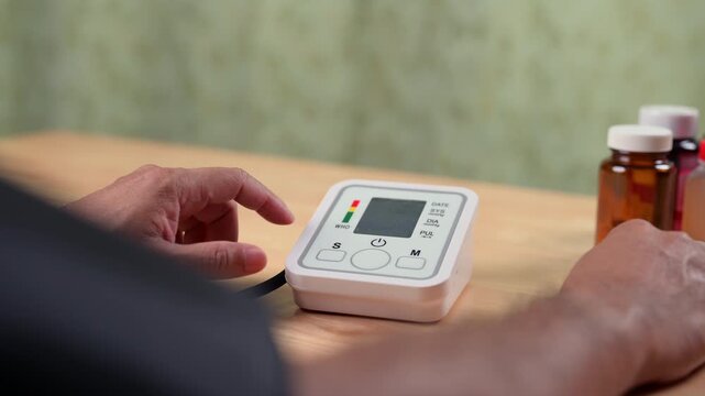Male patient hands prepare digital blood pressure gauge near brown pill vial inside home, managing personal health care, tracking pulse, stopping disease, noting heart rate, keeping body wellness.