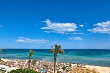 Fototapeta premium Hammamet, Tunisia - MAY 16, 2025: Beach of Hammamet, the first tourist destination in Tunisia. Located on the Gulf of Hammamet. Beach and boats on shallow water, view on Mediterranean sea. Crystal-cle