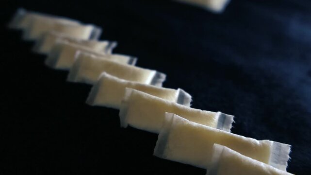 Close up of white nicotine pouches, a popular tobacco alternative, moving in slow motion across a dark surface, highlighting the concept of smokeless nicotine products and addiction
