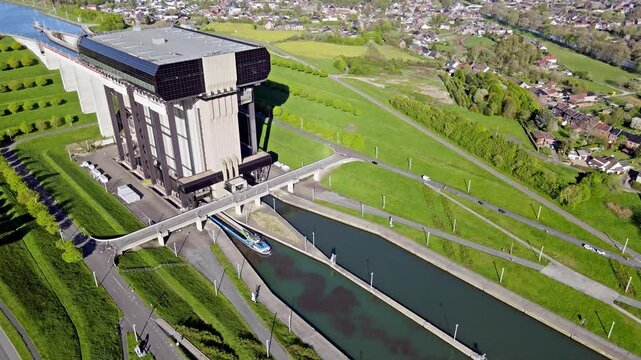 Aerial drone view of cargo barge entering canal lift concrete chamber with green embankments and calm water. Precise mechanical lock operation under clear sky with modern infrastructure visible.