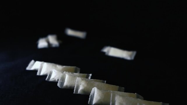 Macro shot of white, non tobacco nicotine pouches arranged in a row with some pouches falling in the background, showcasing a modern alternative to traditional smoking on a dark surface