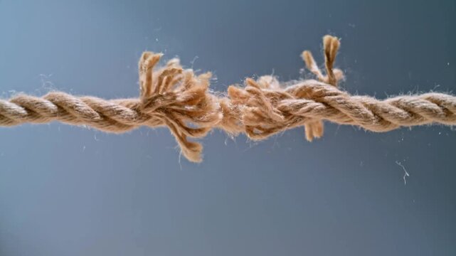 Fraying hemp rope under tension, breaking point of a worn cord, concept of stress and imminent failure in business or relationships