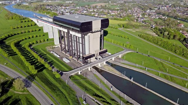 Aerial drone overview of canal boat lift with adjacent water channels and urban environment. Modern infrastructure columns and basin with natural scenery and town structures nearby. Boat lift and