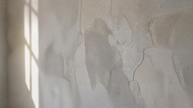  A grey-white wall with interwoven textures of old and new plaster repairs. 