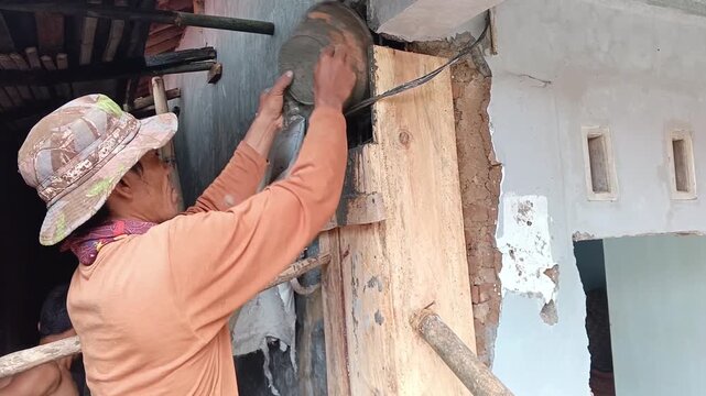 Construction worker pouring concrete into wooden formwork to build a house pillar. Professional manual labor for residential building renovation and structural casting.