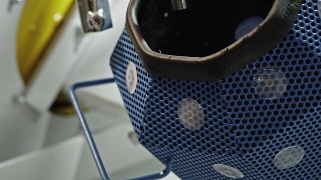 Close up of rotating industrial tumbling drum used for automated deburring and surface finishing of metal components, showcasing precision manufacturing and quality control.
