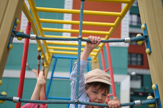 Child playing on playground equipment. Boy climbing on rope net and hanging on monkey bar. Active kid having fun outdoors. Childhood activity, development, movement and exercise concept.