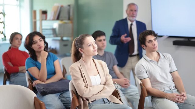 Young girls and guys audience listen to lecture, mature man teacher in background. Social projects for young people. Prevention of addictive behavior, information support for youth in bullying