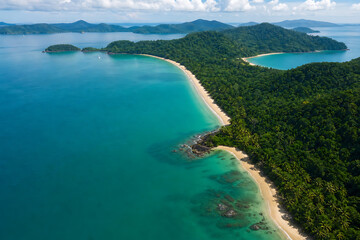 Obraz premium Aerial view of a serene tropical island with lush green forests, white sandy beaches, and crystal clear turquoise waters surrounded by mountains.