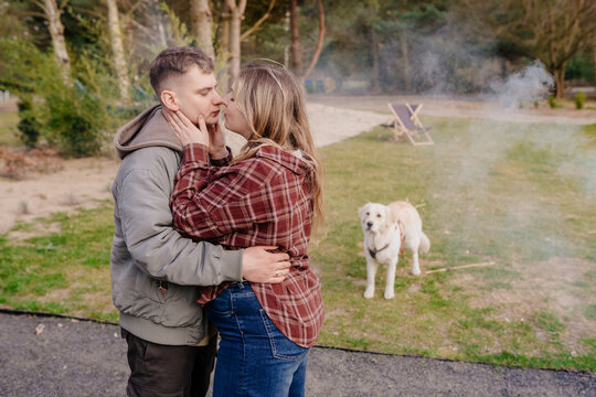 Young white couple kissing outdoors with dog during weekend rest