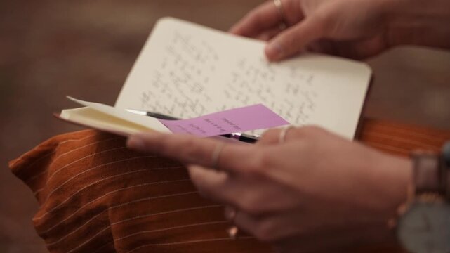 Hands writing in a journal with sticky notes in a natural setting.
