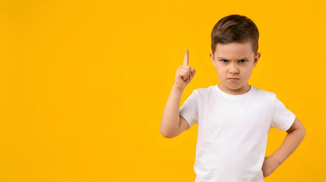 Frustrated young boy with an angry expression pointing his finger upwards and looking at the camera with a stern look